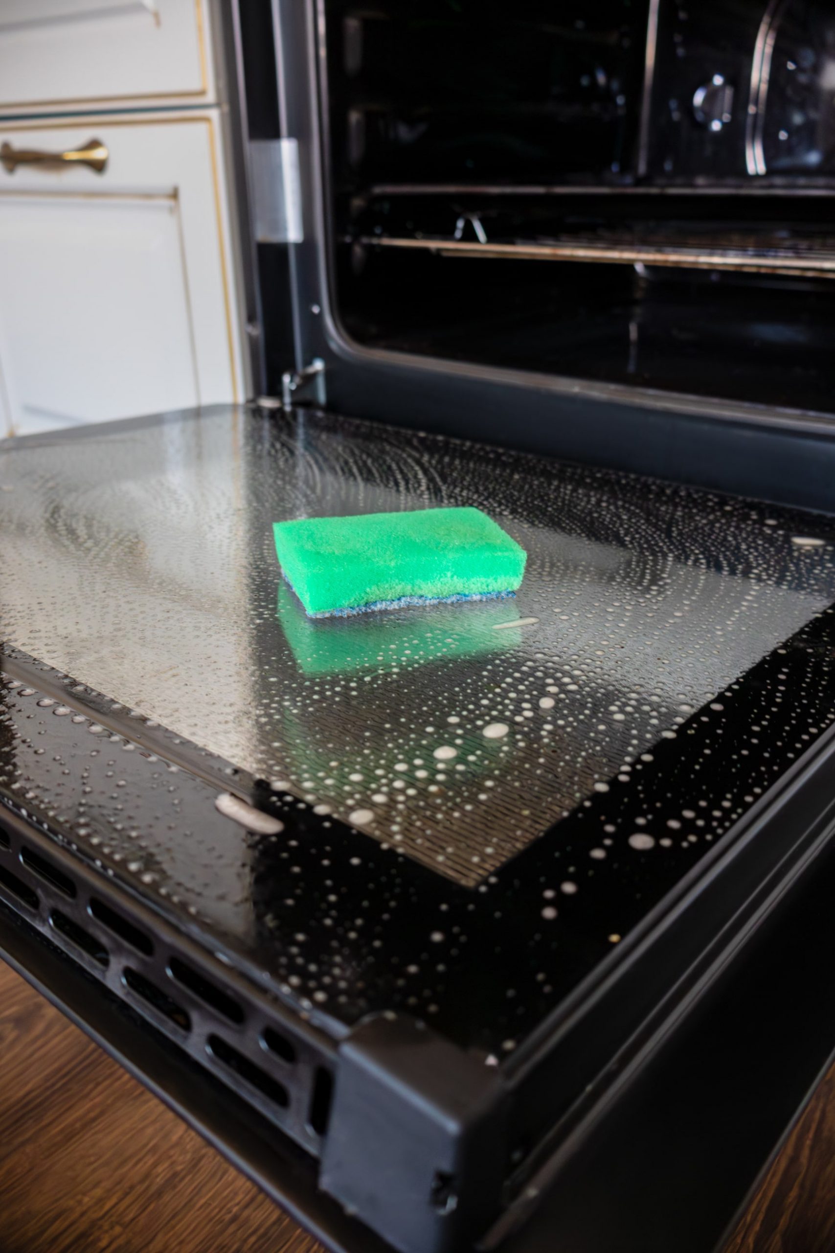 Oven door is lowered down and washed. Sponge for washing lies on its surface<br />
